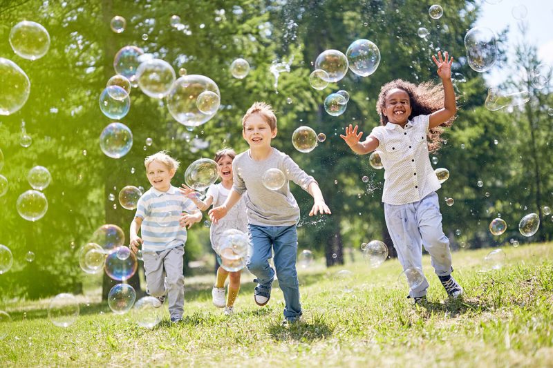 happy children running in grass with bubbles